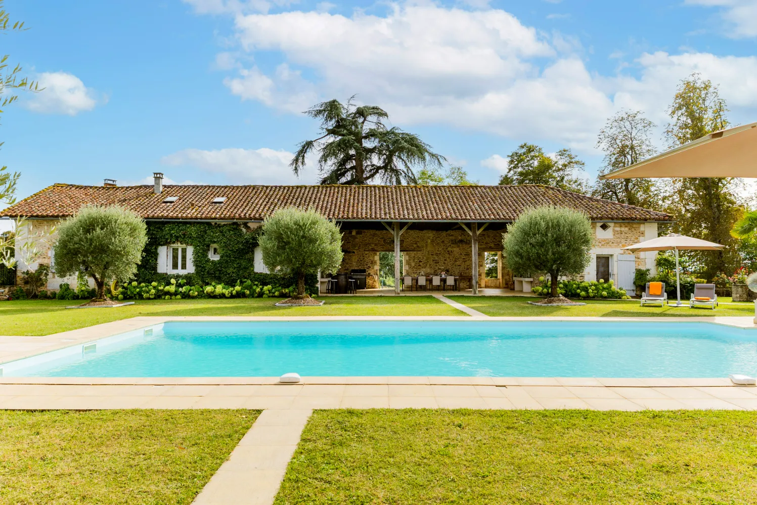 Outdoor pool with lush greenery and a cottage in the background