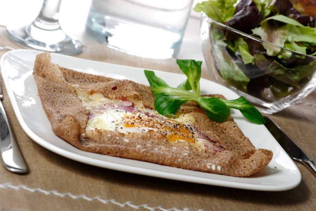 Galette complète with ham, cheese, and egg on a plate, served with fresh salad.
